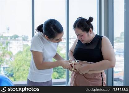 Young female trainer measuring fat layer of overweight woman with caliper at fitness