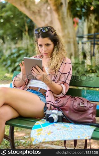 Young female traveler with map and digital tablet in the street, outdoors. Holidays and tourism concept