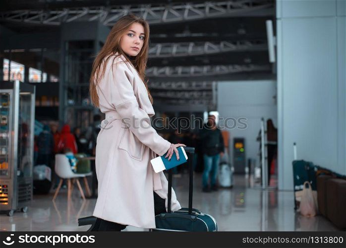 Young female traveller walking the airport hall draging suitcase. Blured airport cafe on the background. Traveller walking the airport hall.