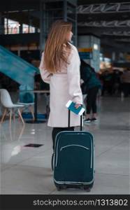 Young female traveller walking the airport hall draging suitcase. Blured airport cafe on the background. Traveller walking the airport hall.