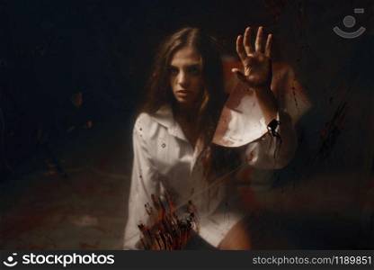 Young female victim with with bloody hands in mental hospital basement. Frightened patient of doctor maniac in clinic for the mentally ill, psychiatrist butcher