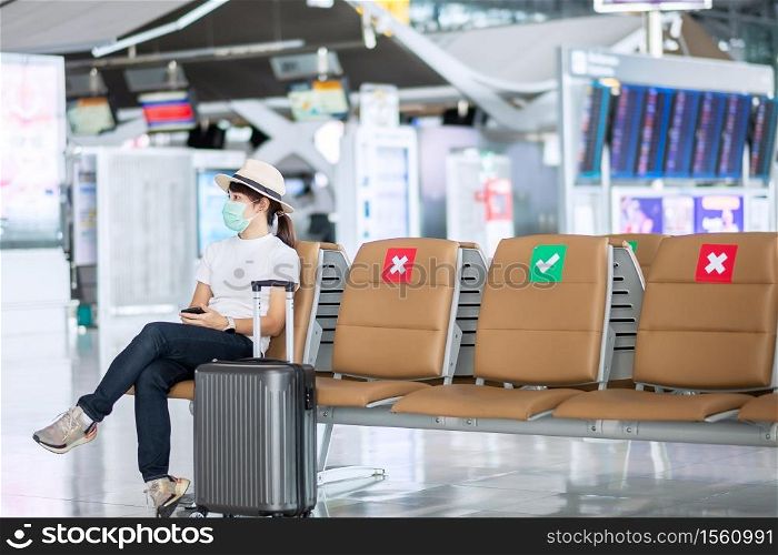 Young female wearing face mask and sitting on chair in airport, protection Coronavirus disease (Covid-19) infection, Asian woman traveler. New Normal, travel bubble and social distancing