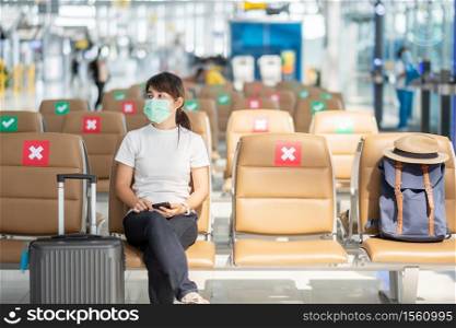 Young female wearing face mask and sitting on chair in airport, protection Coronavirus disease (Covid-19) infection, Asian woman traveler. New Normal, travel bubble and social distancing