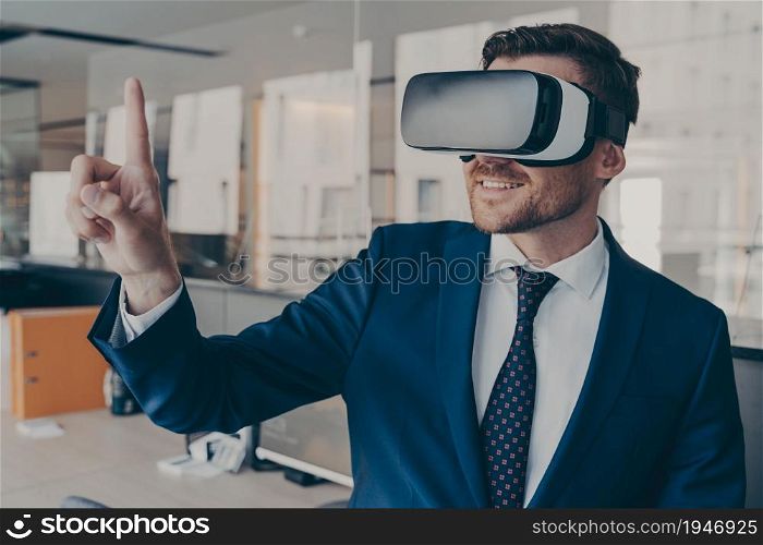 Young financier experiencing immersive virtual reality technology wearing VR glasses, interacting with 360 degrees headset user interface, while standing in his office, selects content in 3D menu. Young financier wearing VR headset glasses, while standing in his office