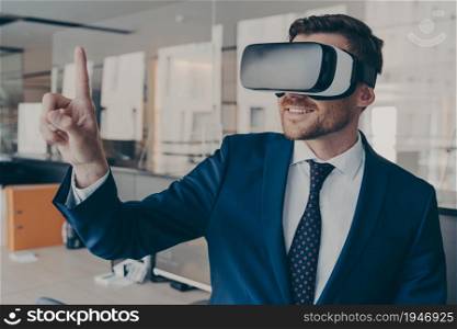 Young financier experiencing immersive virtual reality technology wearing VR glasses, interacting with 360 degrees headset user interface, while standing in his office, selects content in 3D menu. Young financier wearing VR headset glasses, while standing in his office