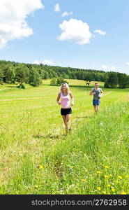 Young fit couple jogging on summer day in meadows countryside