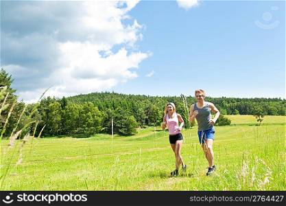 Young fit couple jogging on summer day in meadows countryside