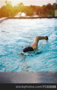 Young fit girl in goggles and cap swimming freestyle stroke in the blue water pool with light, exercise and training lifestyle