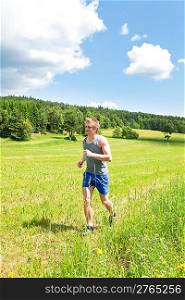 Young fit man jogging on summer day in meadows countryside