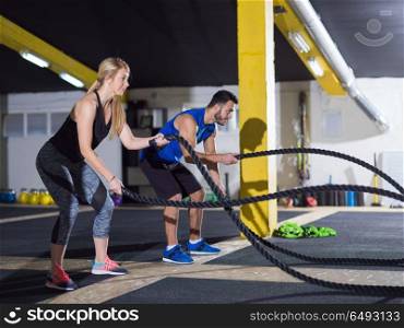young fit sports couple working out in functional training gym doing crossfitness exercise with battle ropes. sports couple doing battle ropes crossfitness exercise