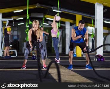 young fit sports couple working out in functional training gym doing crossfitness exercise with battle ropes. sports couple doing battle ropes crossfitness exercise
