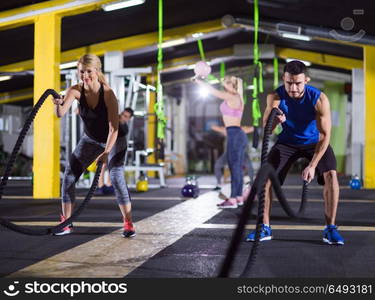 young fit sports couple working out in functional training gym doing crossfitness exercise with battle ropes. sports couple doing battle ropes crossfitness exercise