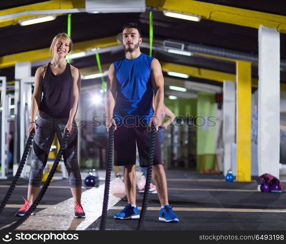 young fit sports couple working out in functional training gym doing crossfitness exercise with battle ropes. sports couple doing battle ropes crossfitness exercise