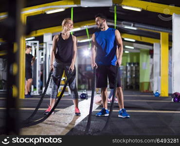 young fit sports couple working out in functional training gym doing crossfitness exercise with battle ropes. sports couple doing battle ropes crossfitness exercise