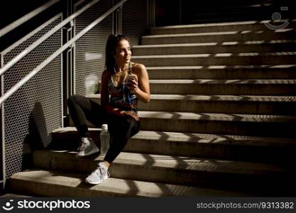 Young fit sporty woman resting and listen music on mobile phone after training outdoor in urban enviroment