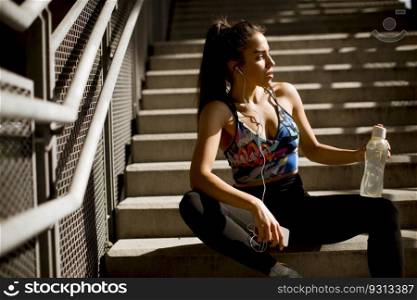 Young fit sporty woman resting and listen music on mobile phone after training outdoor in urban enviroment