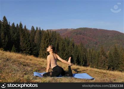 Young fit woman doing exercises on yoga mat on background of sunny mountains hills. Outdoor workout, healthy lifestyle. female in sport suit is stretching in nature against the forest in the morning.. Young fit woman doing exercises on yoga mat on background of sunny mountains hills. Outdoor workout, healthy lifestyle. female in sport suit is stretching in nature against the forest in the morning