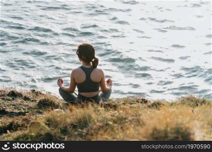 Young fit woman doing yoga in the rocks of a wild coast with the ocean in front during a sunny day with copy space relax and peace concept