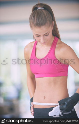 young fit woman measuring belly on a training in fitness gym. young fit woman measuring belly