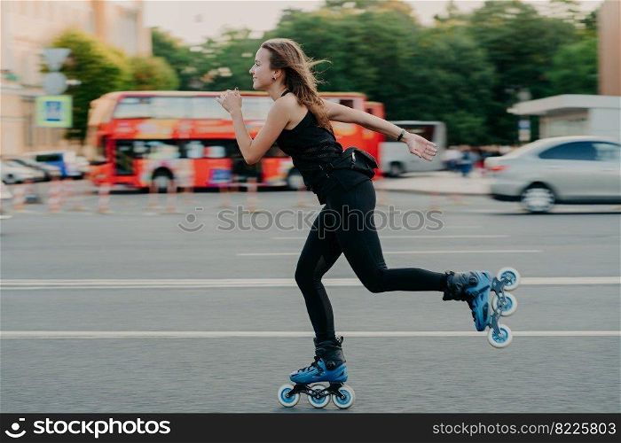 Young fit woman on roller skates with wheels rollerblades during summer day on busy road with transport leads active lifestyle wears black sportsclothes breathes fresh air. Movement concept.