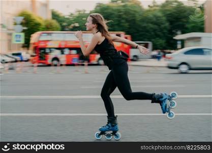 Young fit woman on roller skates with wheels rollerblades during summer day on busy road with transport leads active lifestyle wears black sportsclothes breathes fresh air. Movement concept.