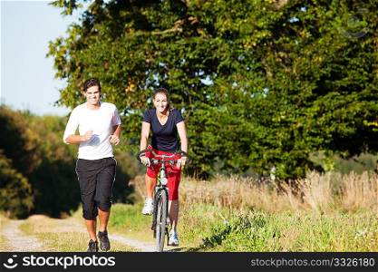 Young fitness couple doing sport outdoors, jogging and riding a bicycle in autumn under a clear blue sky