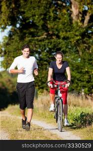 Young fitness couple doing sport outdoors, jogging and riding a bicycle in autumn under a clear blue sky
