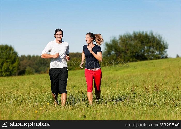 Young fitness couple doing sport outdoors, jogging on a green summer meadow in the grass under a clear blue sky