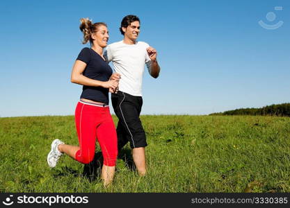 Young fitness couple doing sport outdoors, jogging on a green summer meadow in the grass under a clear blue sky