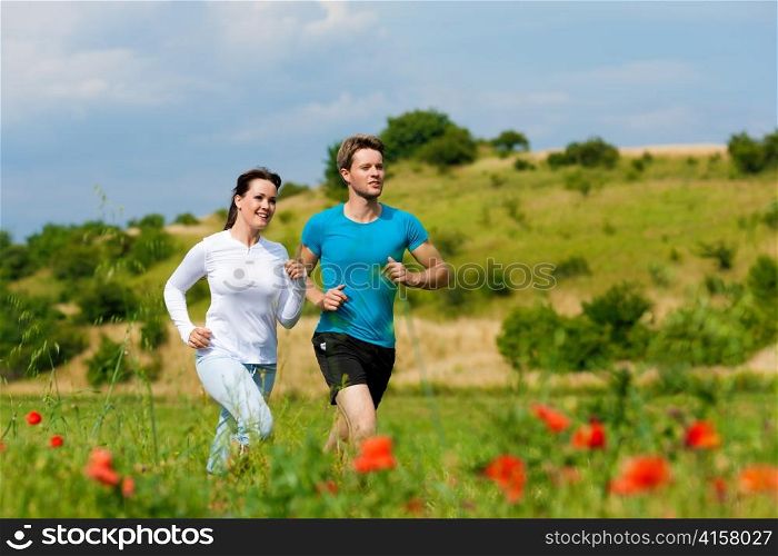 Young fitness couple doing sports outdoors; jogging on a green meadow in summer under a blue sky