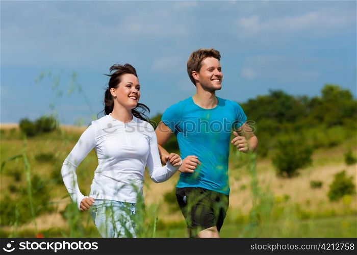 Young fitness couple doing sports outdoors; jogging on a green meadow in summer under a blue sky