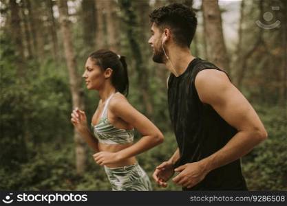 Young fitness couple running at the forest trail on a summer day