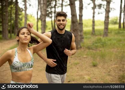 Young fitness couple running at the forest trail on a summer day