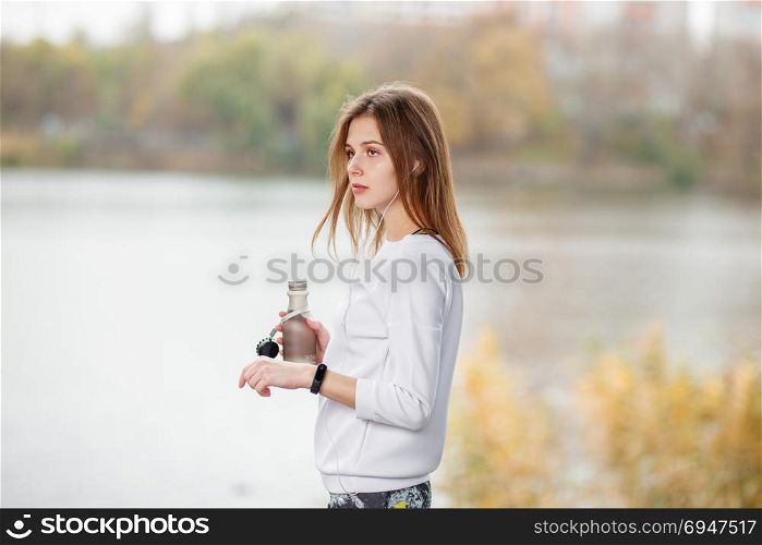 Young fitness girl with bottle of water standing outdoor in city park.. Young fitness girl with bottle of water standing outdoor in city park