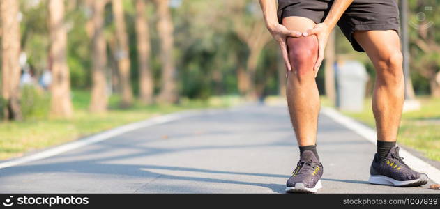 Young fitness man holding his sports leg injury. muscle painful during training. Asian runner having knee ache and problem after running and exercise outside morning. sport and healthy concepts