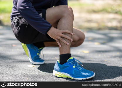 Young fitness man holding his sports leg injury, muscle painful during training. Asian runner having calf ache and problem after running and exercise outside in summer