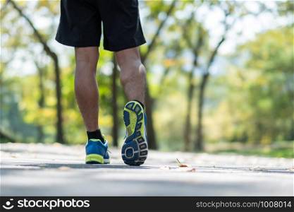 young fitness man legs walking in the park outdoor, male runner running on the road outside, asian athlete jogging and exercise on footpath in sunlight morning. Sport,healthy and wellness concepts