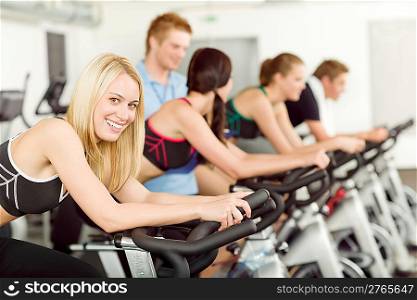 Young fitness people doing spinning with instructor at gym