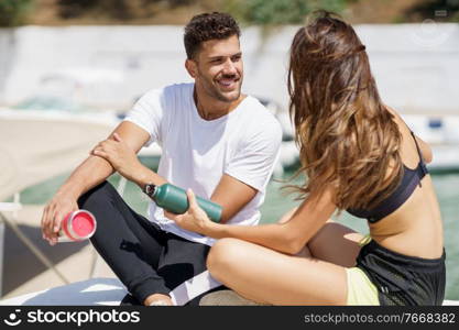 Young fitness people hydrate themselves with water in metal bottles while taking a break after sport.. Young sporting couple hydrate themselves with water in metal cans while taking a break after sport.
