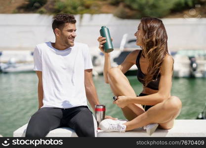 Young fitness people hydrate themselves with water in metal bottles while taking a break after sport.. Young sporting couple hydrate themselves with water in metal cans while taking a break after sport.