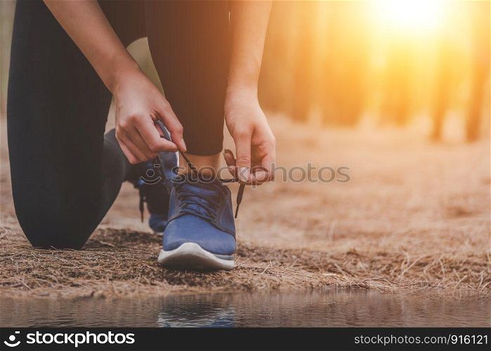 Young fitness running woman tying shoelaces at outdoors in forest background. Sport and Nature concept. Countryside Exercise and and Athlete Activity concept. Healthy and Lifestyle theme.