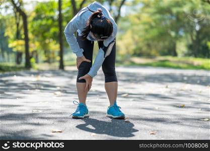 Young fitness woman holding his sports leg injury, muscle painful during training. Asian runner having calf ache and problem after running and exercise outside in summer