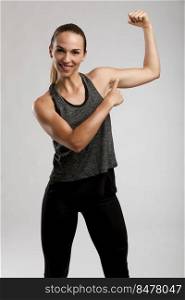 Young fitness woman pointing to her muscle and smiling