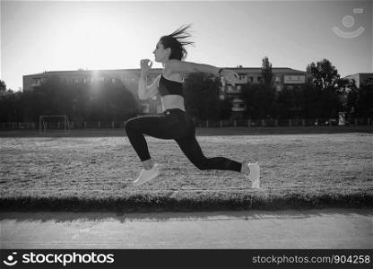 Young fitness woman runner running on stadium track.The concept of a healthy lifestyle and sports.. Young woman running during sunny morning on stadium track