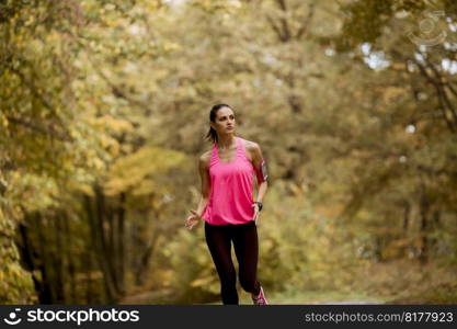 Young fitness woman running at  forest trail in autumn