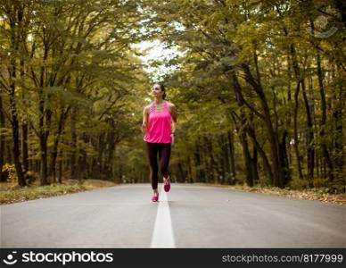 Young fitness woman running at forest trail in golden autumn