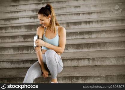 Young fitness woman taking a break from running sitting on steps and suing mobile phone in armband