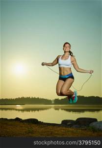 Young fitness woman used a skipping rope, sun and sea on background, copy space