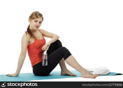 young fitness woman with a bottle of water sitting on a mat. young fitness woman with a bottle of water sitting on a mat making a break on white background