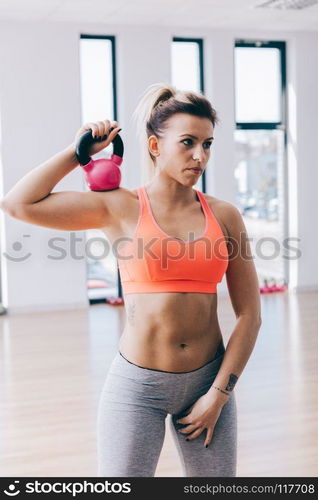 Young fitnesswoman holding and training with a kettle. Fit lifestyle. Gym equipment.. Young fitnesswoman training with a kettle